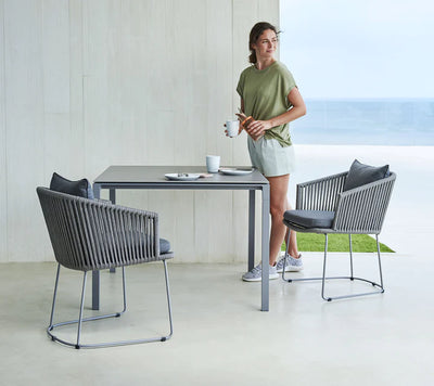 Woman standing next to a square table and two chairs on white patio