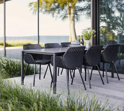 Dark grey dining set on a grey wooden deck with a body of water in the background