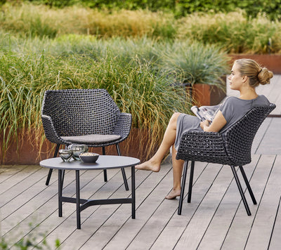 Woman sitting on armchair by grasses and shown on a wooden deck