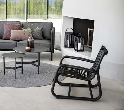 Black woven armchair in front of outdoor fireplace and a gray couch and matching coffee tables