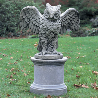 Gray owl spreading its wings on top of a round pedestal