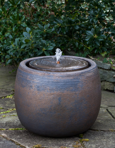 Low round glazed fountain with small bubbler pictured against green foliage
