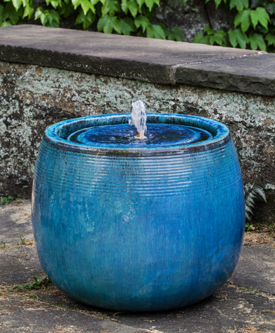 Round blue fountain with small bubbler pictured against stone wall