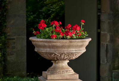Light brown cast stone urn with leaves details shown planted with red geraniums
