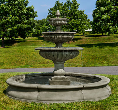 Three tier fountain inside large basin pictured on grass with large trees in the background
