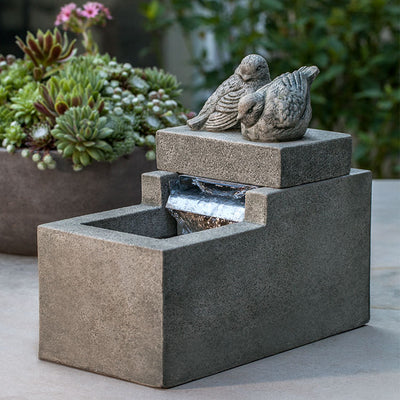Tabletop fountain with two birds sitting on top of back, shown running in front of succulent bowl