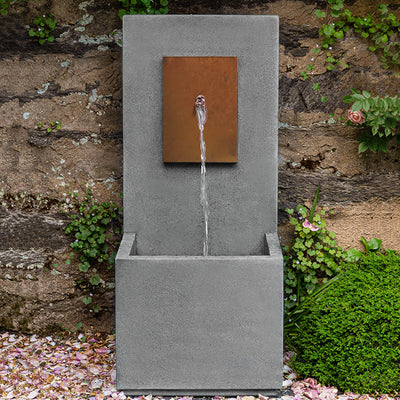 Tall wall fountain with spout coming out of core ten plaque, pictured in front of stone wall