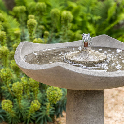 Detail of running birdbath fountain in front of greenery