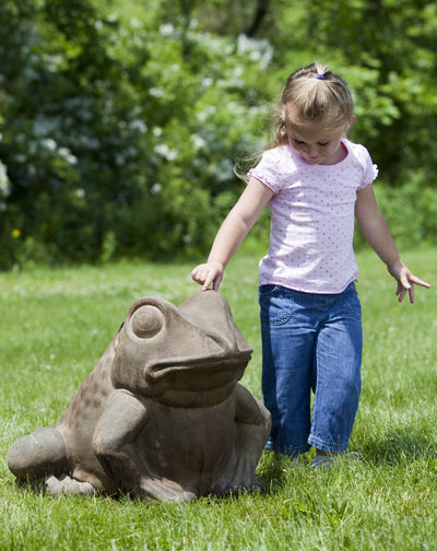 Giant light brown frog sitting on grass with little girl touching its head