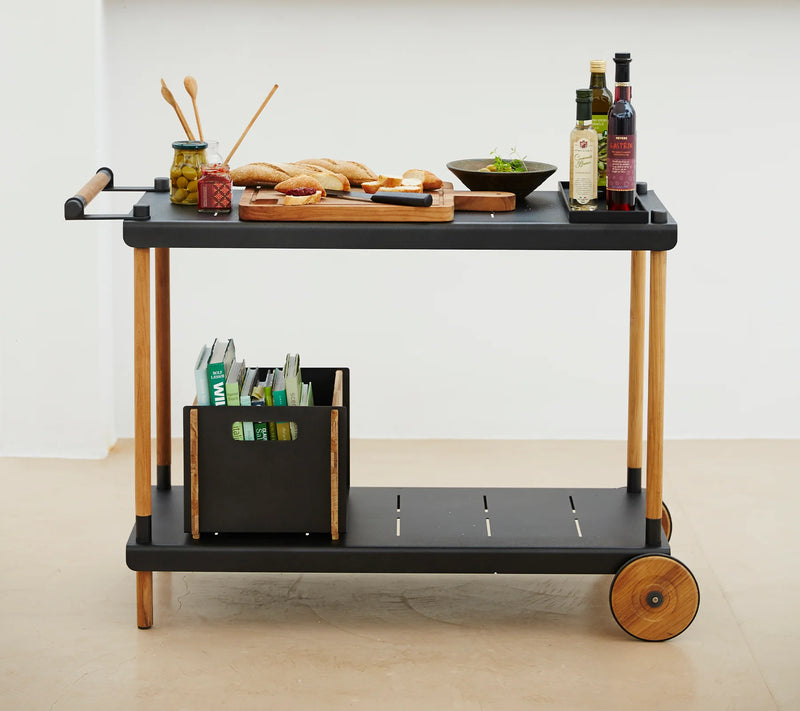 Black trolley with food and bottles against white wall