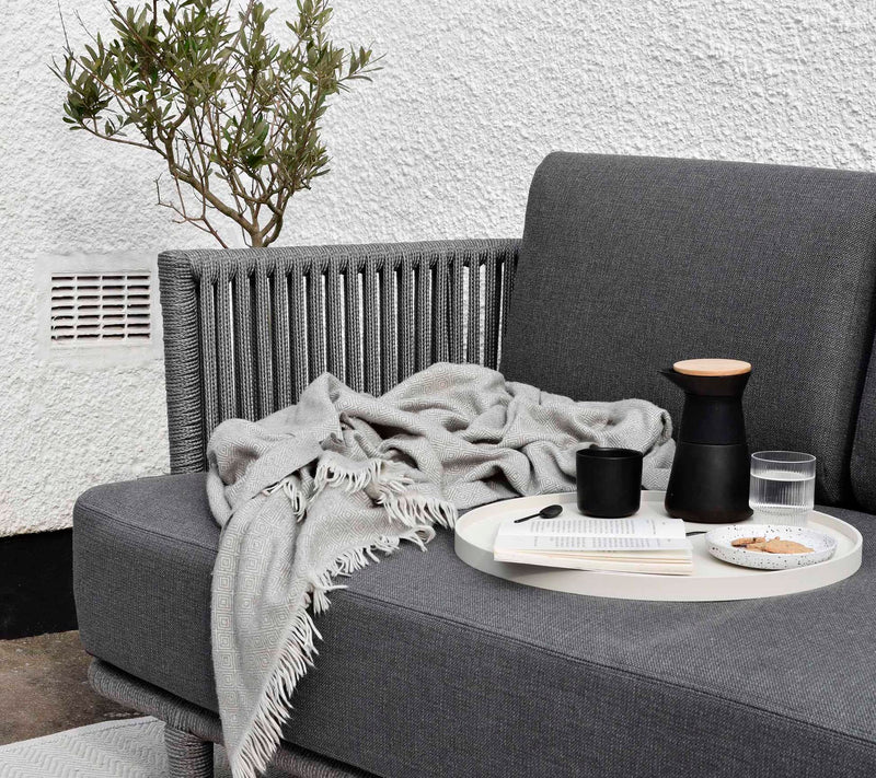 Outdoor sofa with a tray and throw blanket in front of white wall