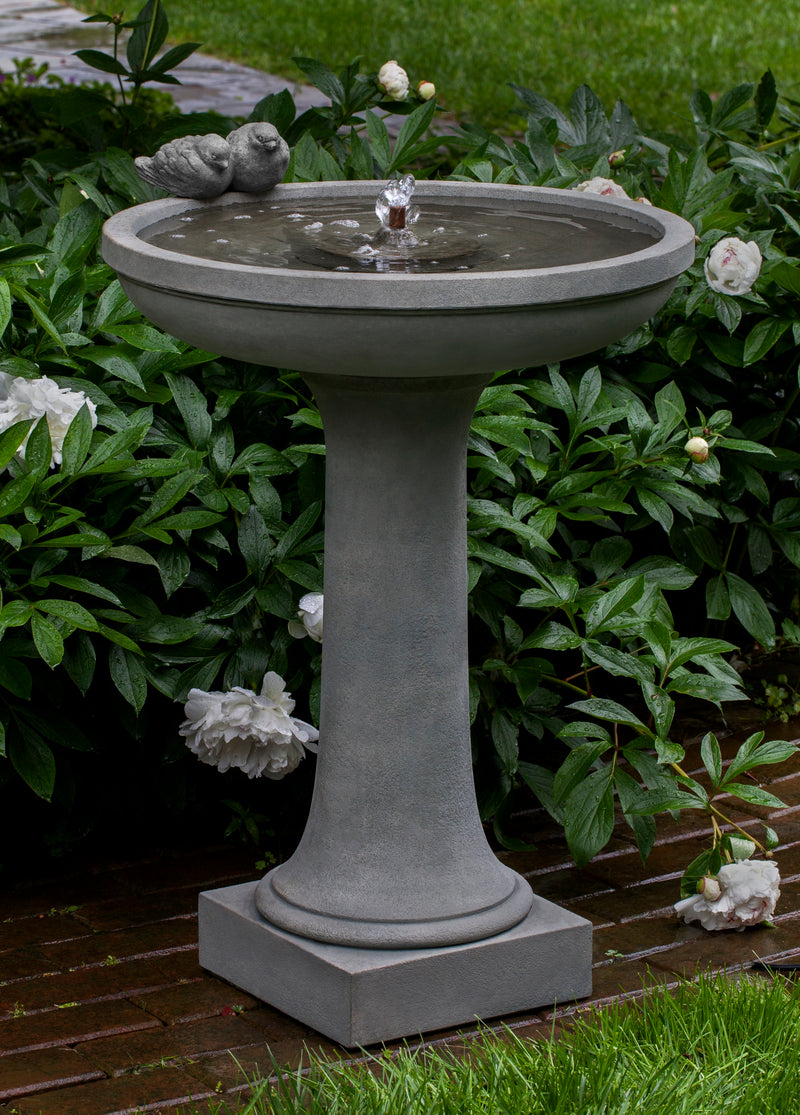 Shallow bowl birdbath fountain with two birds sitting on the side pictured in front of white peonies
