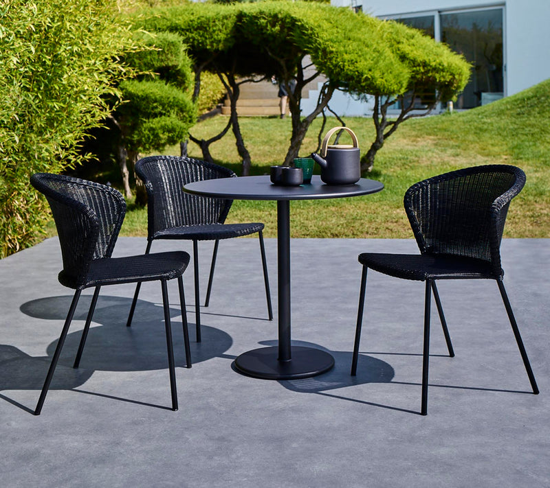 Small black table with three matching armchairs with tea set on top of table