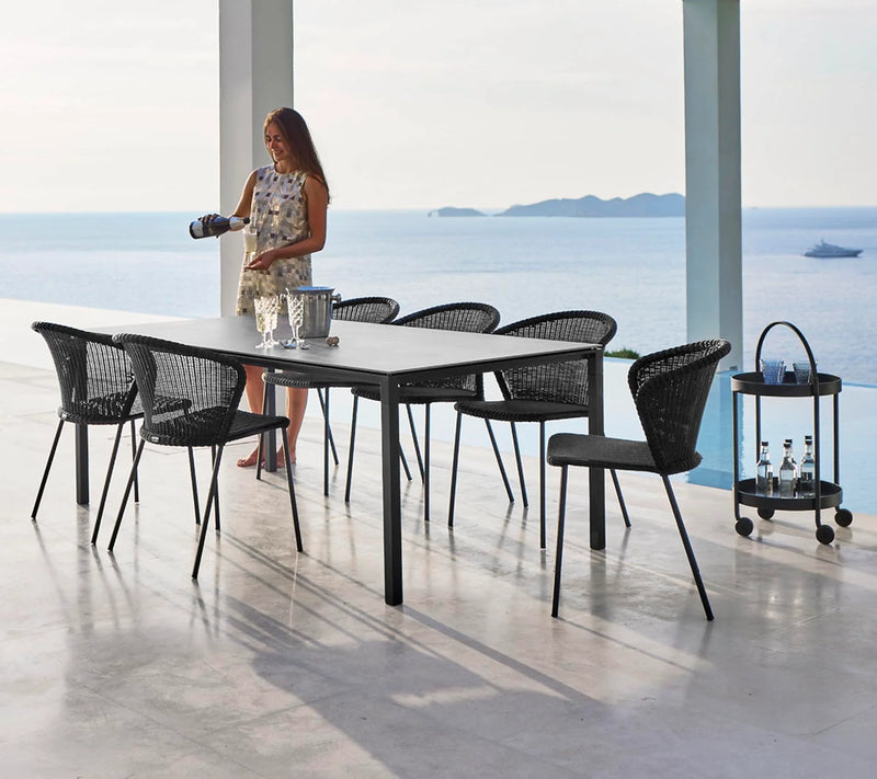 Rectangular table with matching chairs and woman pouring a drink in front of the ocean