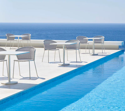 Sets of white square tables and grey chairs shown by a poolside