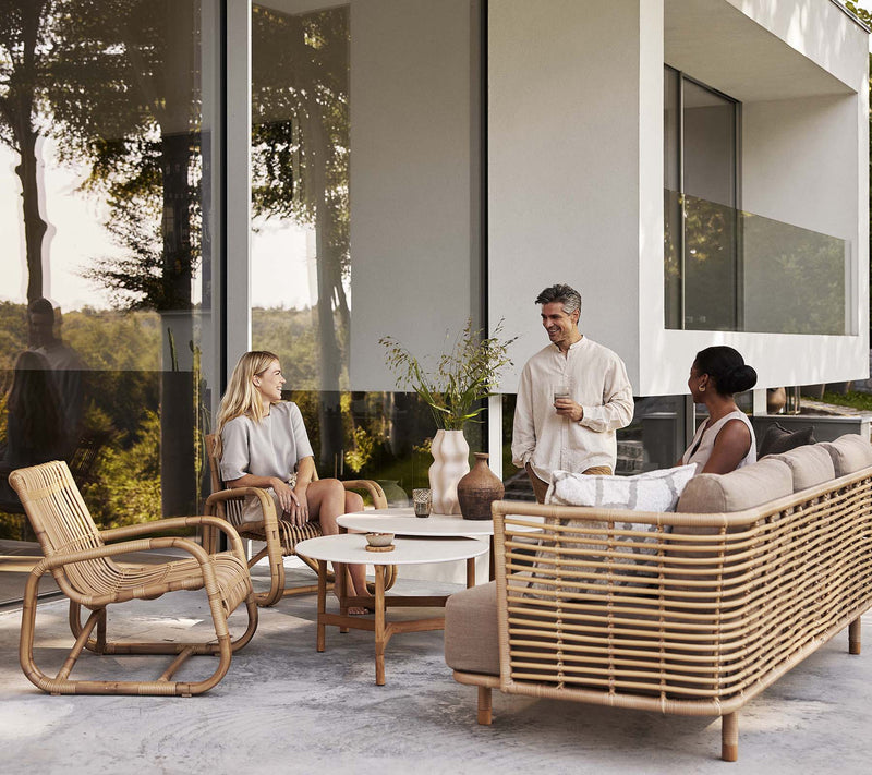 Friends sitting on beige outdoor furniture in front of white and glass house