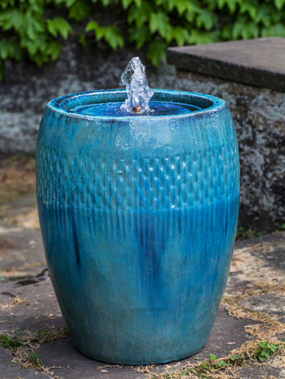Blue glazed fountain with pattern on top half pictured in front of stone wall