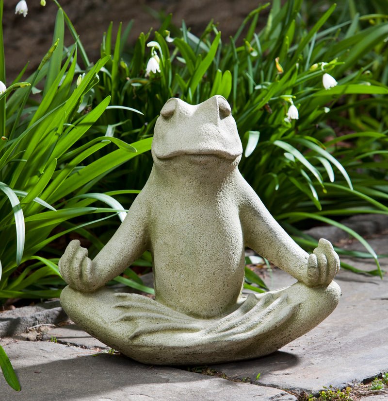 Light green frog sitting in yoga pose in front of greenery