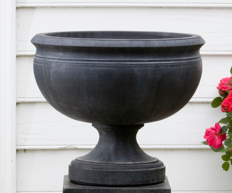 Black urn shown in front of a white wall next to roses