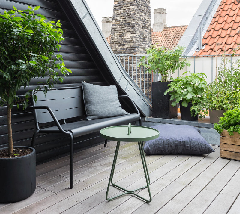 Metal bench with a cushion behind a green coffee table on roof top deck