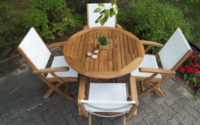 Round teak table with four white armchairs shown on brick pavers patio