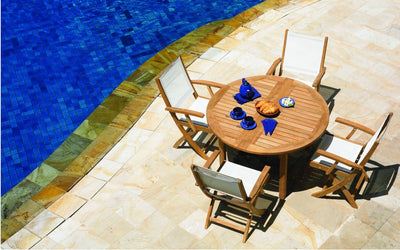Round teak table with four white chairs shown by a pool