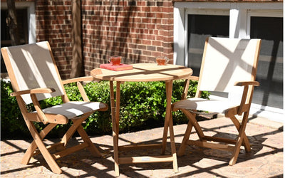 Round teak table with two white armchairs shown in front of brick house