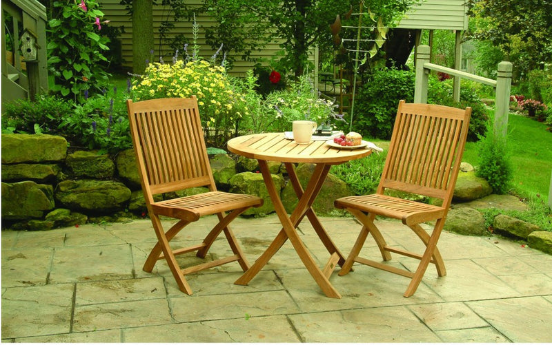 Bistro teak table with two chairs shown on patio in front of lush garden