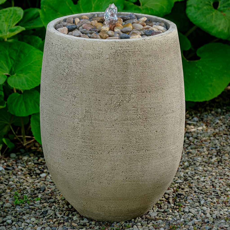 Small grey fountain in vertical oval shape with copper spout and gravel on top