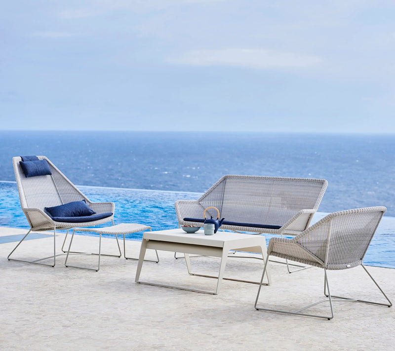 Set of gray woven outdoor furniture including one couch and two armchairs with a coffee table in front of a pool