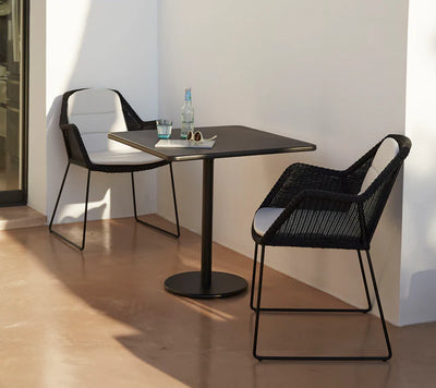 Bistro table with two black armchairs against white wall