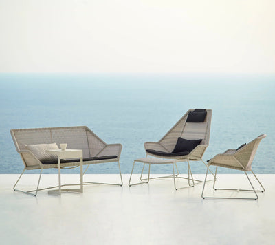Sofa, chairs and stool on white terrace with ocean in the background
