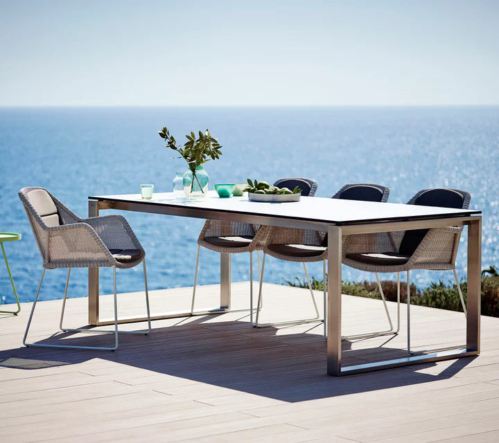 Rectangular table with four chairs shown on a deck by the ocean