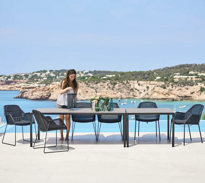 Rectangular table with six chairs shown with a woman installing a lantern by the ocean