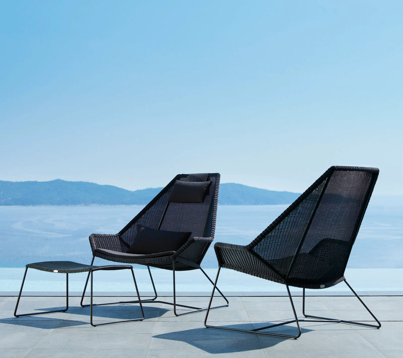 Two black contemporary armchairs with footstool in front of ocean