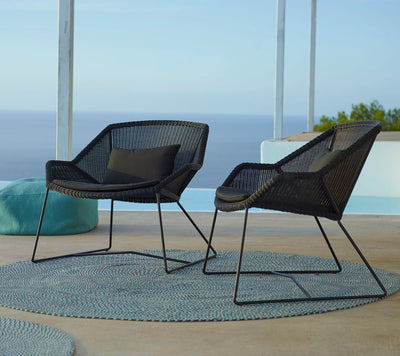 Two contemporary black woven outdoor armchairs on top of gray rug by the ocean
