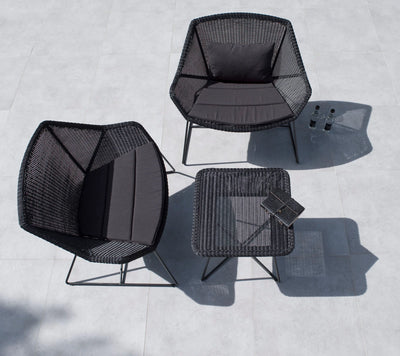 Top view of two black woven outdoor chairs with a matching coffee table on gray terrace