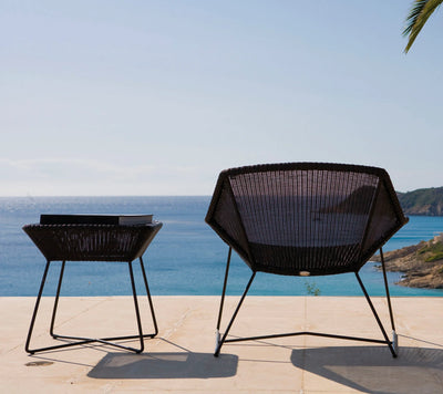 Black woven outdoor armchair next to a matching coffee table in front of ocean