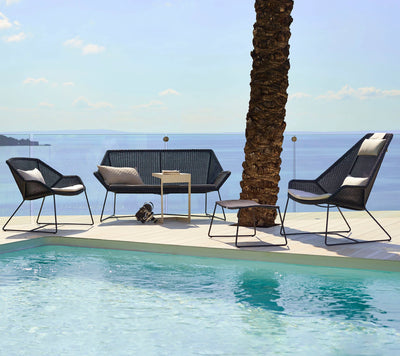 Sofa and two chairs with pool in front and body of water in the background
