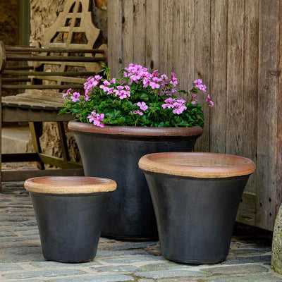 Grouping of 3 dark grey containers with one planted with pink geraniums