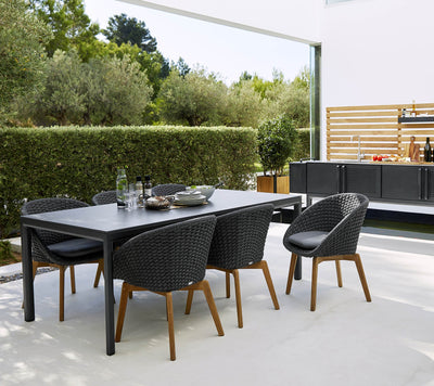 Black dining set in front of outdoor kitchen next to a green hedge