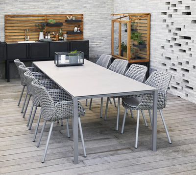 Rectangular grey table with ten chairs in front of white wall and grey deck