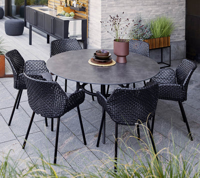 Dining set with black round table and six matching chairs shown with grasses in the foreground