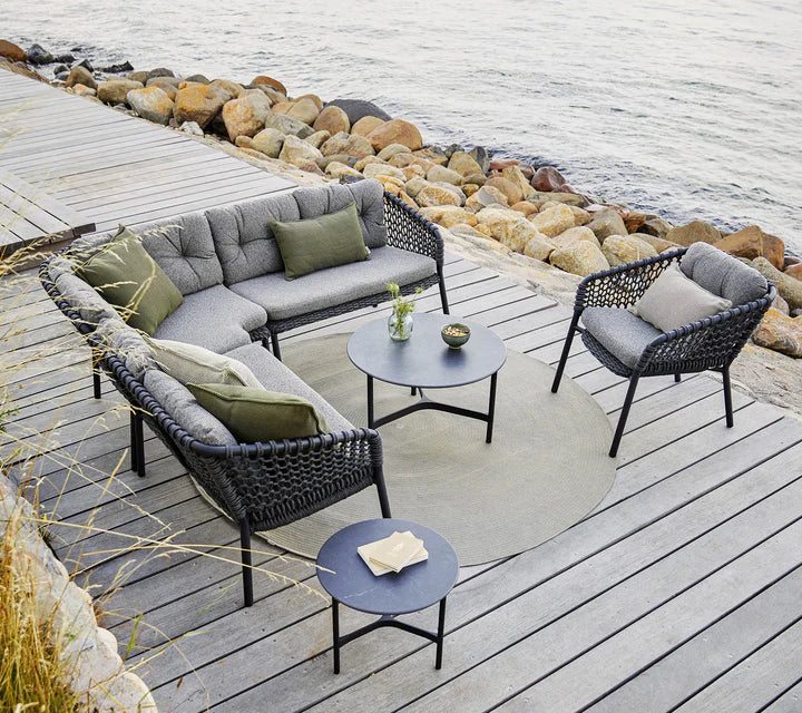 Corner sitting couch with coffee tables and armchair on gray decking by the ocean