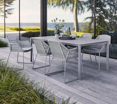 Gray rectangular table and six chairs shown on gray deck by the ocean
