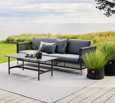 Gray couch and coffee table on light gray rug by the ocean