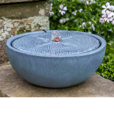 Baby blue tabletop fountain with patterned top pictured in front of pink flowers