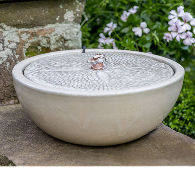 Cream tabletop fountain with patterned top pictured in front of pink flowers