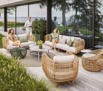 Three people lounging on an outdoor furniture set in front of glass walls