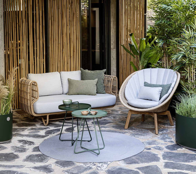 Outdoor sofa and chair in front of bamboo wall next to tropical plants